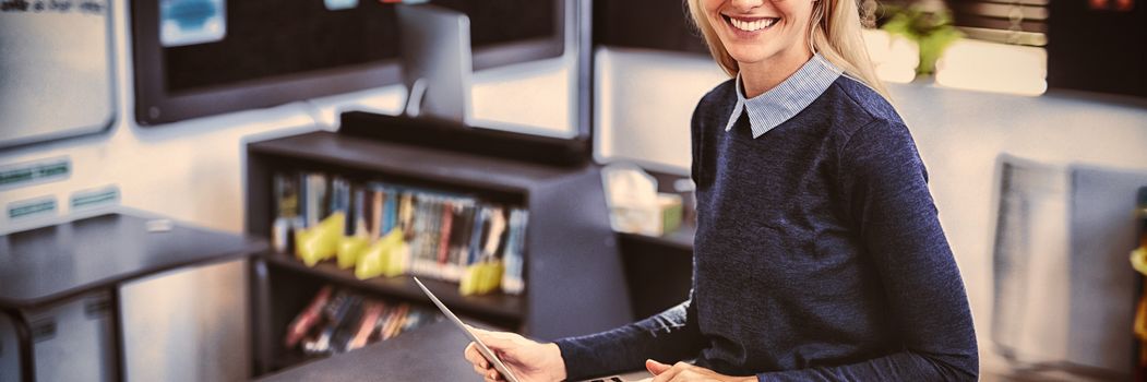 Portrait of happy teacher using laptop in classroom at school