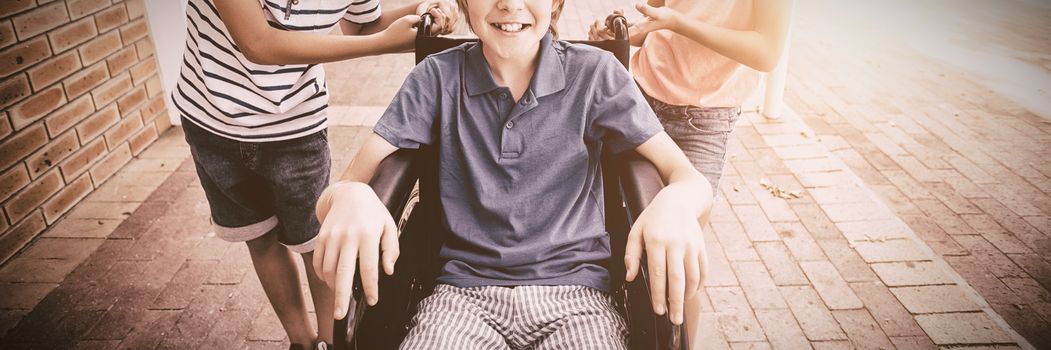 Portrait of school kids pushing a boy on wheelchair at school corridor