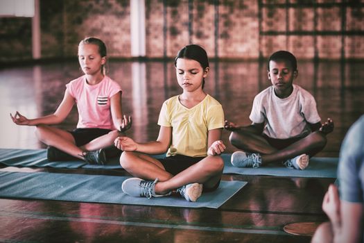 School kids meditating during yoga class in basketball court at school gym