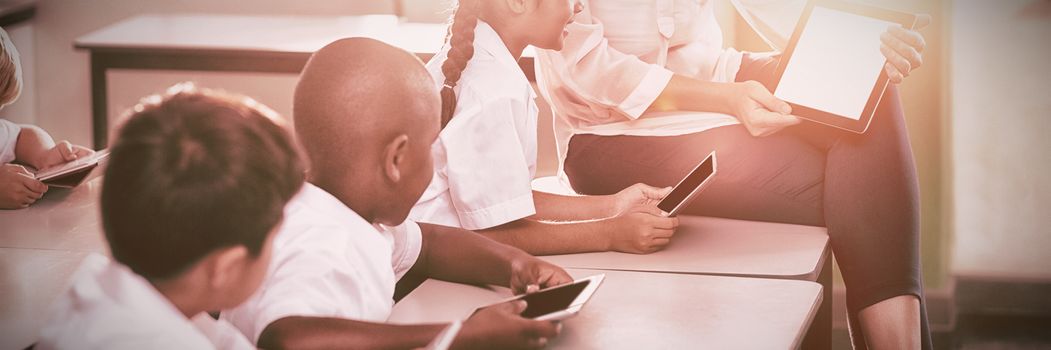 Teacher teaching kids on digital tablet in classroom at school