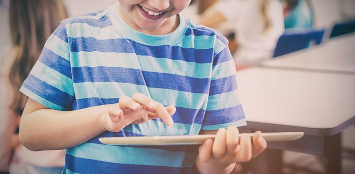 Smiling schoolboy using digital tablet while standing in classroom at elementary school