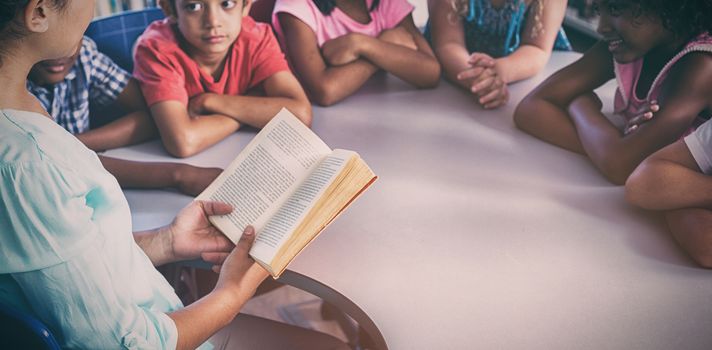 Female teacher reading book at children look at her library