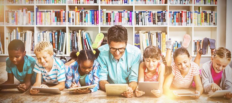 Teacher and kids lying on floor using digital tablet in library at school