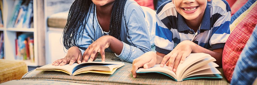 Portrait of school kids lying on sofa and reading book in library