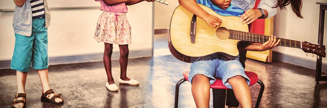 Teacher assisting a kids to play a musical instrument in classroom at school