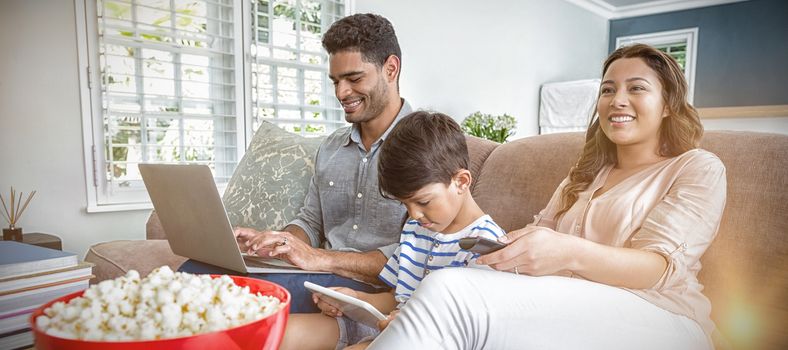 Mother watching television while father and son using laptop and digital tablet at home