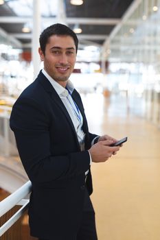 Portrait close-up of handsome Caucasian businessman looking at camera while working on mobile phone in a modern office. International diverse corporate business partnership concept