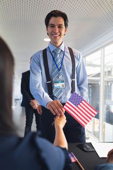 Front view of caucasian Happy Businessman holding an American flag at conference registration table. International diverse corporate business partnership concept