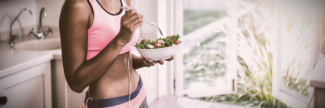 Happy woman having bowl of salad while listening to music in kitchen