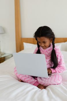 Front view of African american girl using laptop on bed in bedroom at home