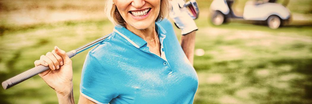 Portrait of happy mature woman carrying golf club while standing on field