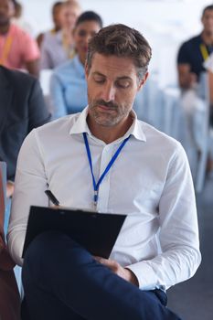 Close-up of caucasian businessman writing on clipboard in a business seminar. International diverse corporate business partnership concept