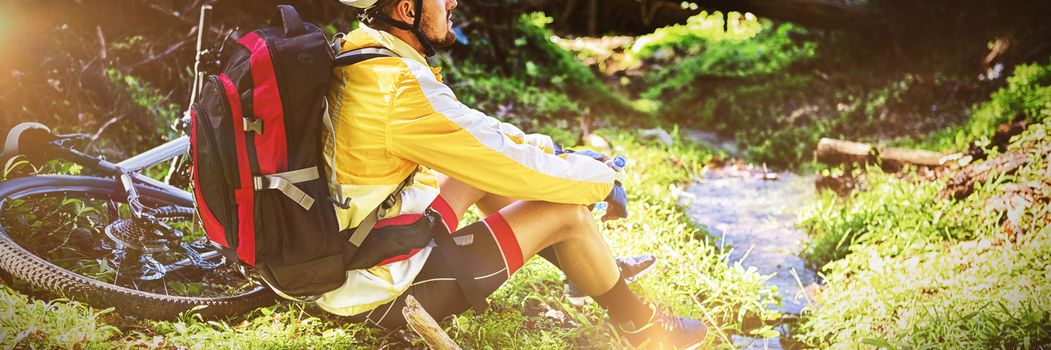 Mountain biker sitting near stream and looking at nature in forest