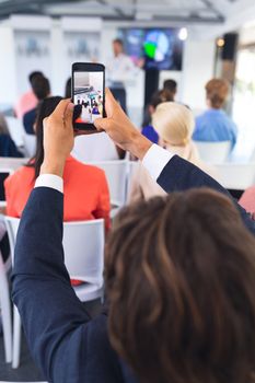 Close-up of caucasian Businessman clicking photo of business seminar with mobile phone in conference meeting. International diverse corporate business partnership concept