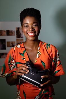Portrait of pretty young African-american female graphic designer holding virtual reality headset in office. This is a casual creative start-up business office for a diverse team.