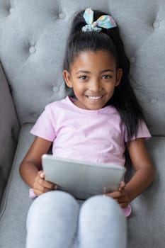 Front view of African american Girl using digital tablet on a sofa in living room at home