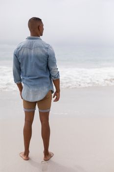 Rear view of thoughtful African american man looking at sea on the beach