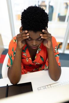 High view of stressed young African american female graphic designer sitting at desk in office. This is a casual creative start-up business office for a diverse team