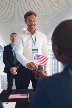 Front view of caucasian Happy Businessman holding an American flag at conference registration table. International diverse corporate business partnership concept