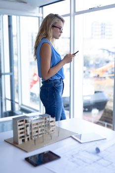 Side view of Caucasian female architect using mobile phone in a modern office. This is a casual creative start-up business office for a diverse team