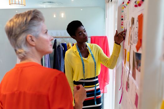 Side view of diverse female fashion designers discussing together over sketch design in design studio. This is a casual creative start-up business office for a diverse team