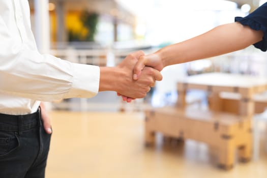 Mid section close-up of Caucasian business people shaking hands with each other in corridor at office. International diverse corporate business partnership concept