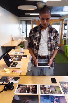 Front view of handsome mixed race male graphic designer using digital tablet at desk in office. This is a casual creative start-up business office for a diverse team