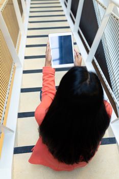 High angle view of pretty young Asian businesswoman using digital tablet on stairs in office. This is a casual creative start-up business office for a diverse team