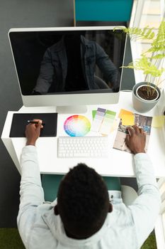 High angle view of African american male graphic designer using graphic tablet at desk in office. This is a casual creative start-up business office for a diverse team