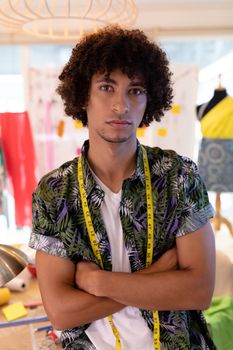 Portrait of handsome young mixed race male fashion designer sitting with arms crossed in design studio. This is a casual creative start-up business office for a diverse team