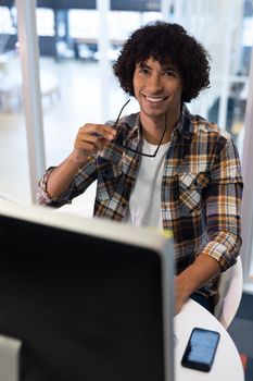 Portrait of young mixed-race male graphic designer smiling at desk in office. This is a casual creative start-up business office for a diverse team