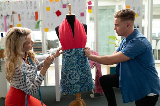 Side view of Caucasian fashion designers dressing mannequin in design studio. This is a casual creative start-up business office for a diverse team