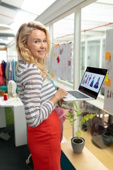 Portrait of young Caucasian female fashion designer using laptop in design studio. This is a casual creative start-up business office for a diverse team