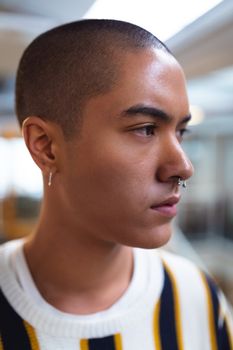 Side view of thoughtful mixed race male graphic designer standing in office. This is a casual creative start-up business office for a diverse team