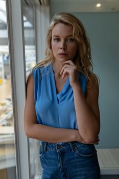 Front view of beautiful Caucasian businesswoman looking at camera while standing near window in office. This is a casual creative start-up business office for a diverse team