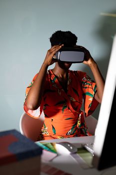 Side view of pretty young African american female graphic designer using virtual reality headset at desk in office. This is a casual creative start-up business office for a diverse team