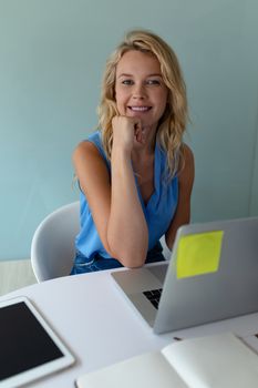 Front view of happy Caucasian businesswoman looking at camera while working at desk in office. This is a casual creative start-up business office for a diverse team