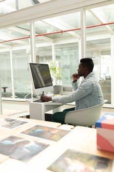 Side view of African american male graphic designer using graphic tablet at desk in office. This is a casual creative start-up business office for a diverse team