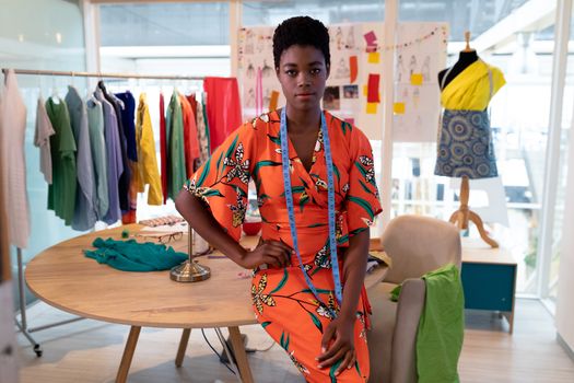 Portrait of young pretty African american female fashion designer sitting with hand on hip in design studio. This is a casual creative start-up business office for a diverse team
