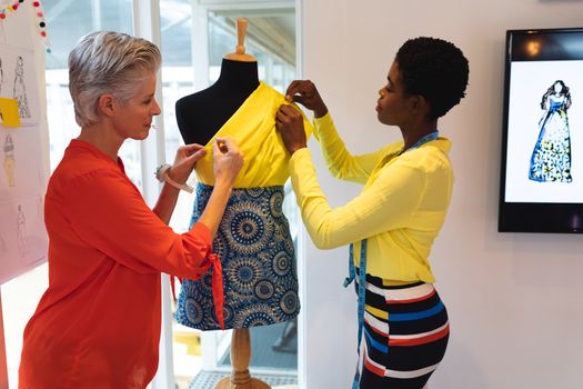 Side view of diverse female fashion designers using measuring tape on a mannequin in design studio. This is a casual creative start-up business office for a diverse team