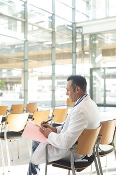 Side view mature male executive sat empty in conference room thinking while writing on folder