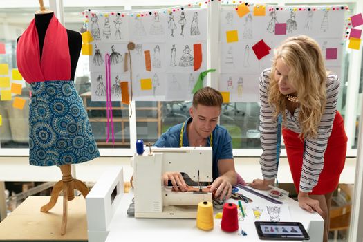 Front view of Caucasian male fashion designer using sewing machine on a table in design studio. This is a casual creative start-up business office for a diverse team