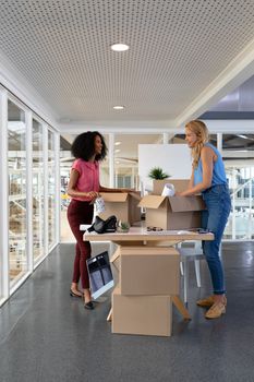 Side view of young diverse female executives unpacking cardboard boxes in office. This is a casual creative start-up business office for a diverse team