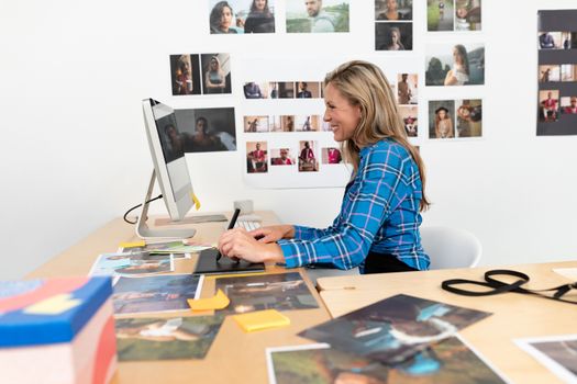 Side view of mature Caucasian female fashion designer using graphic tablet at desk in office. This is a casual creative start-up business office for a diverse team