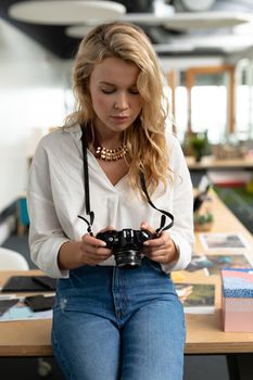 Close-up of Caucasian female graphic designer reviewing photos on digital camera in a modern office. This is a casual creative start-up business office for a diverse team