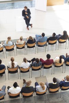 Overhead view of diverse executives sat in conference room, looking speech