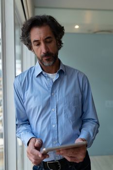 Front view of Caucasian businessman working on digital tablet while standing near window in office. This is a casual creative start-up business office for a diverse team