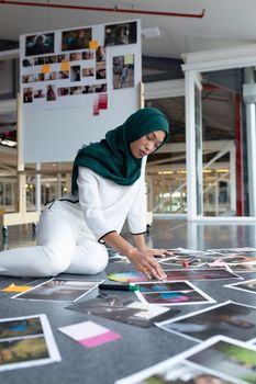 Side view of young mixed race female graphic designer in hijab checking photographs in office. This is a casual creative start-up business office for a diverse team