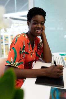 Portrait of young African american female graphic designer working on graphic tablet at desk. This is a casual creative start-up business office for a diverse team