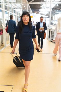 Front view of Asian businesswoman walking with luggage in corridor at office  with business people. International diverse corporate business partnership concept